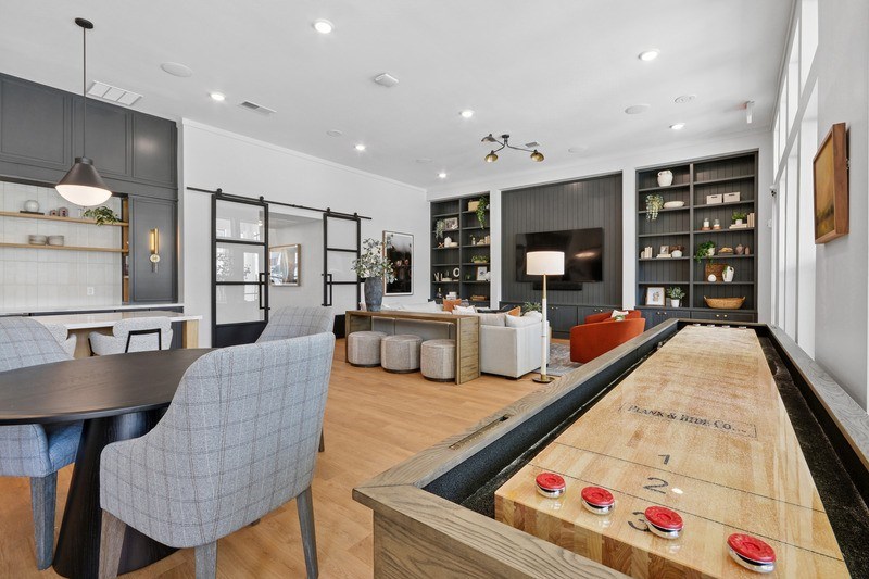 A shiny wooden table with a billiard table in the middle of a room with grey chairs.