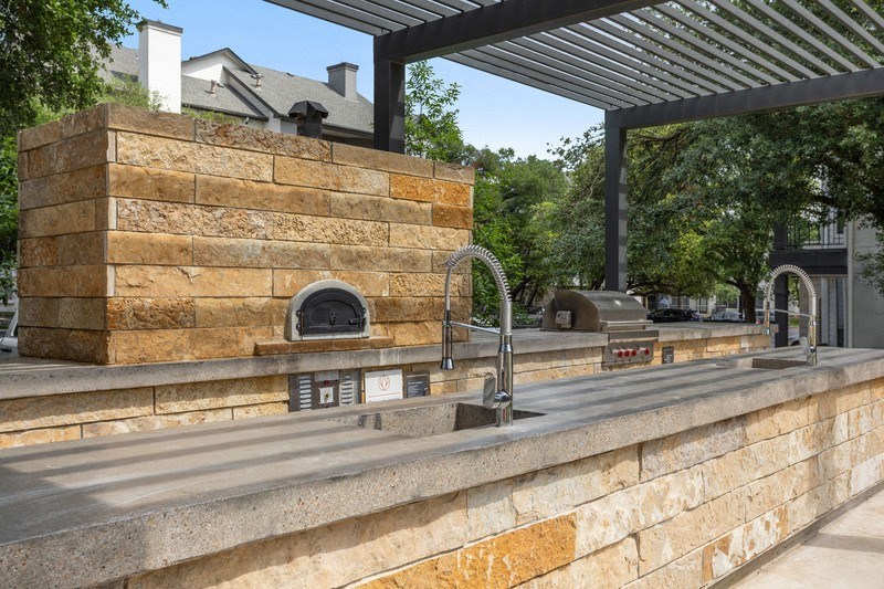 a patio with a stone wall and an outdoor kitchen with a woodfired pizza oven