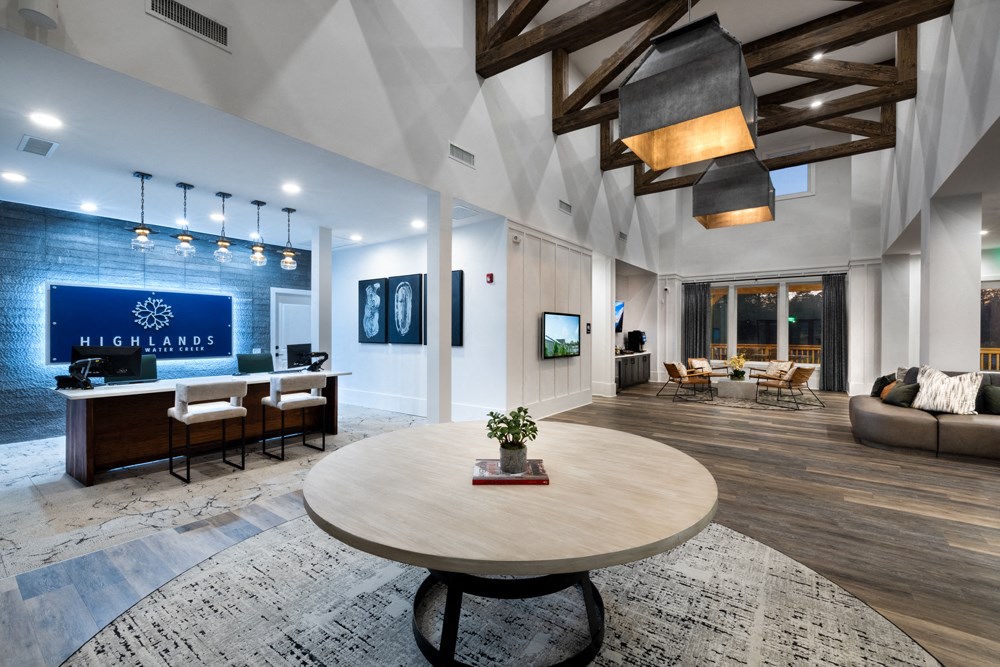 A large, round wooden table is at the center of a spacious room with a high ceiling and wooden beams.