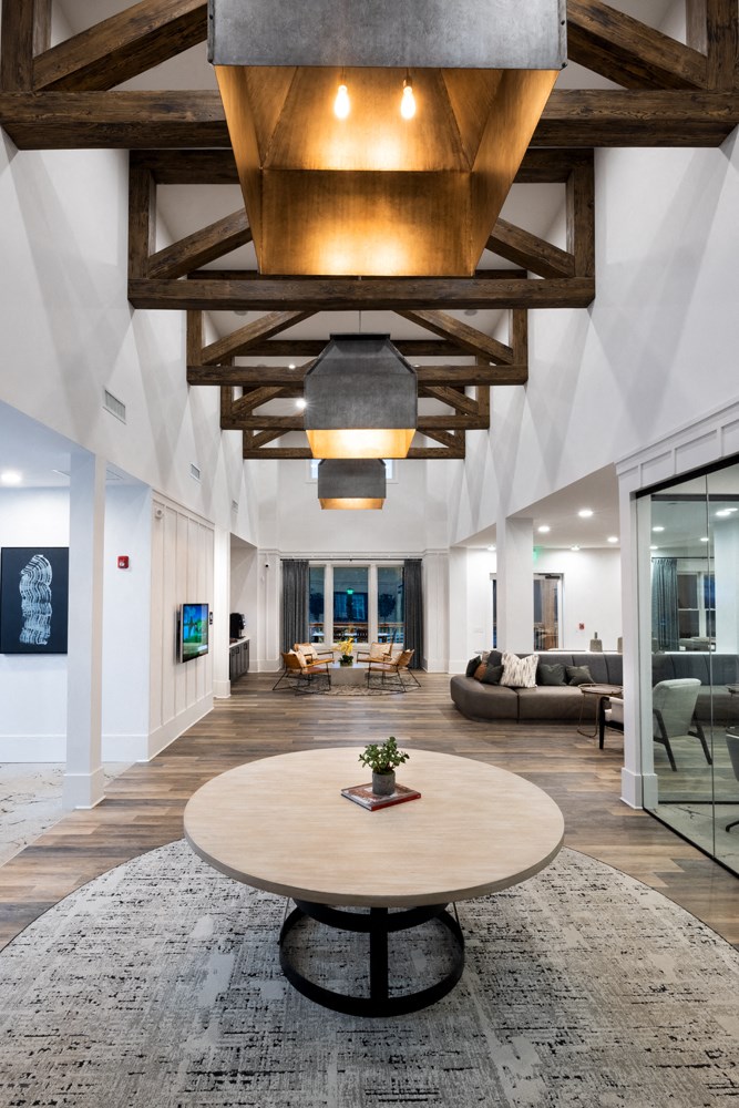 A large, open living room with a wooden table in the center and a glass door leading to a balcony.