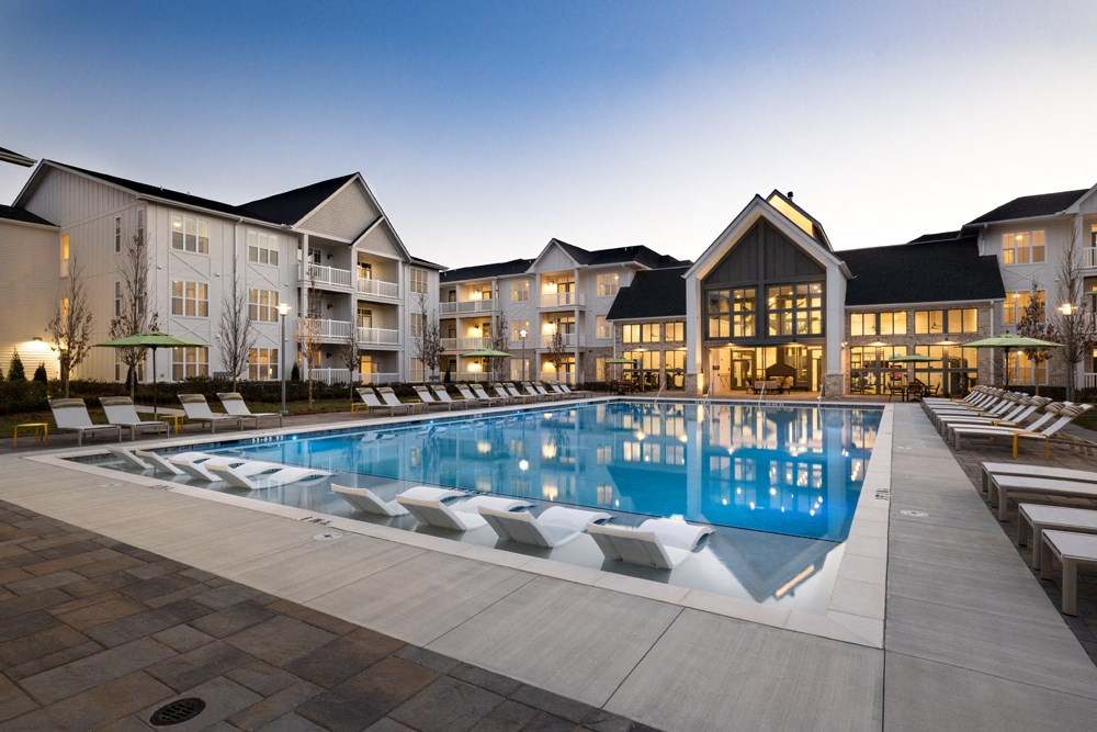 A large swimming pool in front of a building with lounge chairs around it.