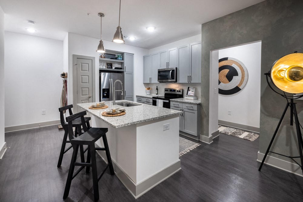 A modern kitchen with a white island and black chairs.