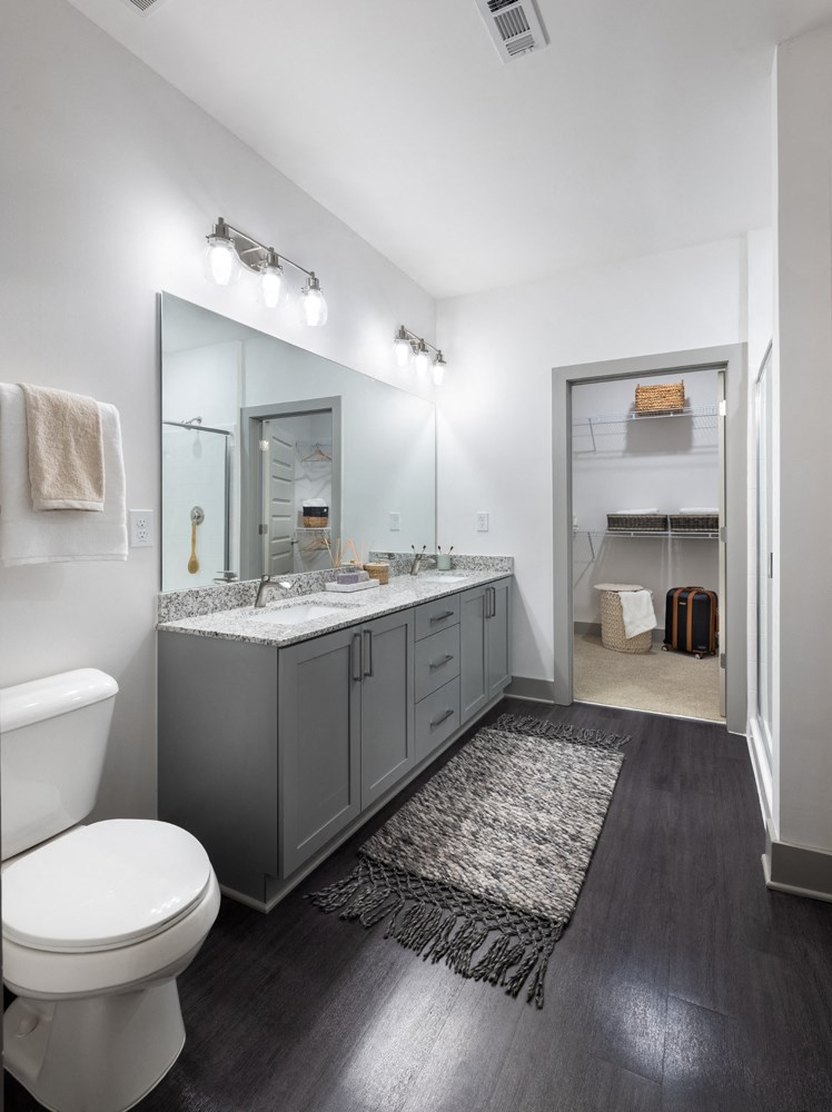A bathroom with a white toilet, a large mirror, and a wooden floor.