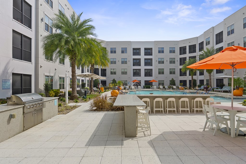 A sunny day at the poolside with orange umbrellas and palm trees.