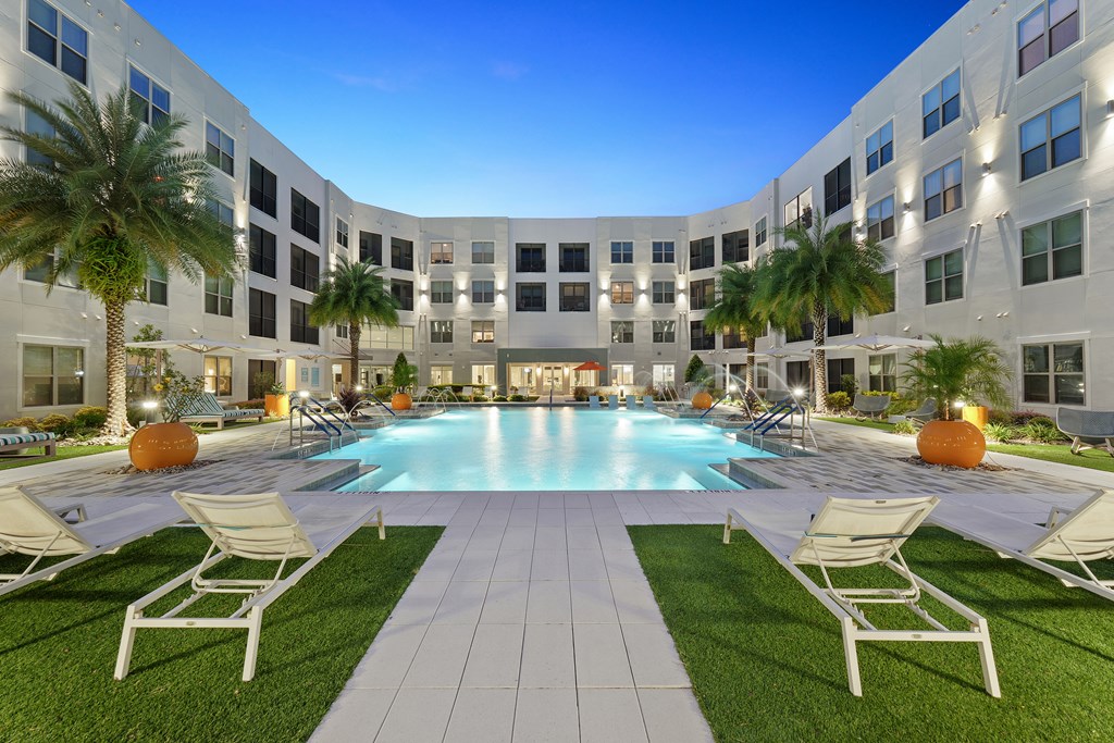 A large white building with a pool in the middle of a grassy area.