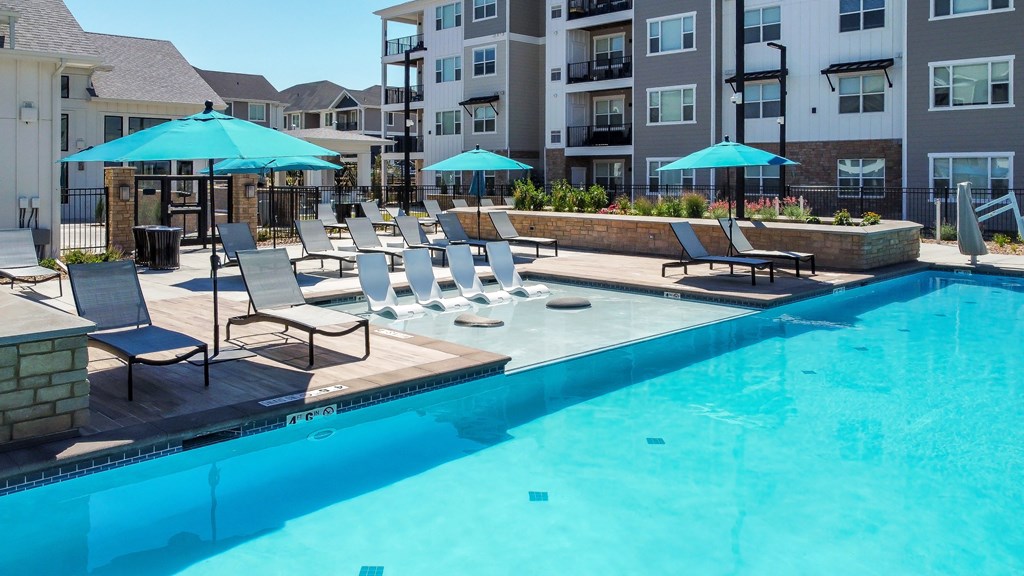 a swimming pool with chairs and umbrellas in front of an apartment building