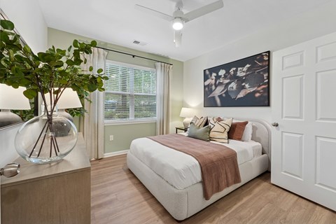 A bedroom with a bed, window, ceiling fan, dresser and a painting on the wall.