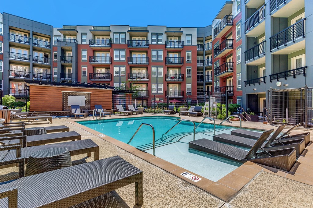 a swimming pool with lounge chairs in front of an apartment building