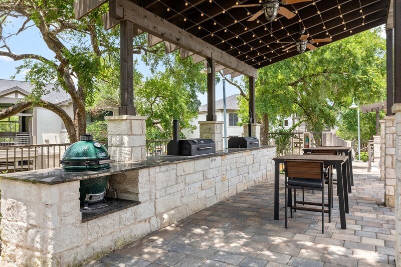 an outdoor kitchen with a grill and a pergola with trees in the background