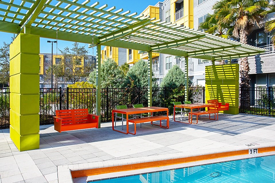 A pool area with a yellow and green pergola and orange furniture.