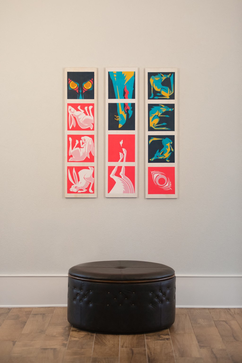 a grouping of three prints hanging on a wall with a black ottoman in the foreground