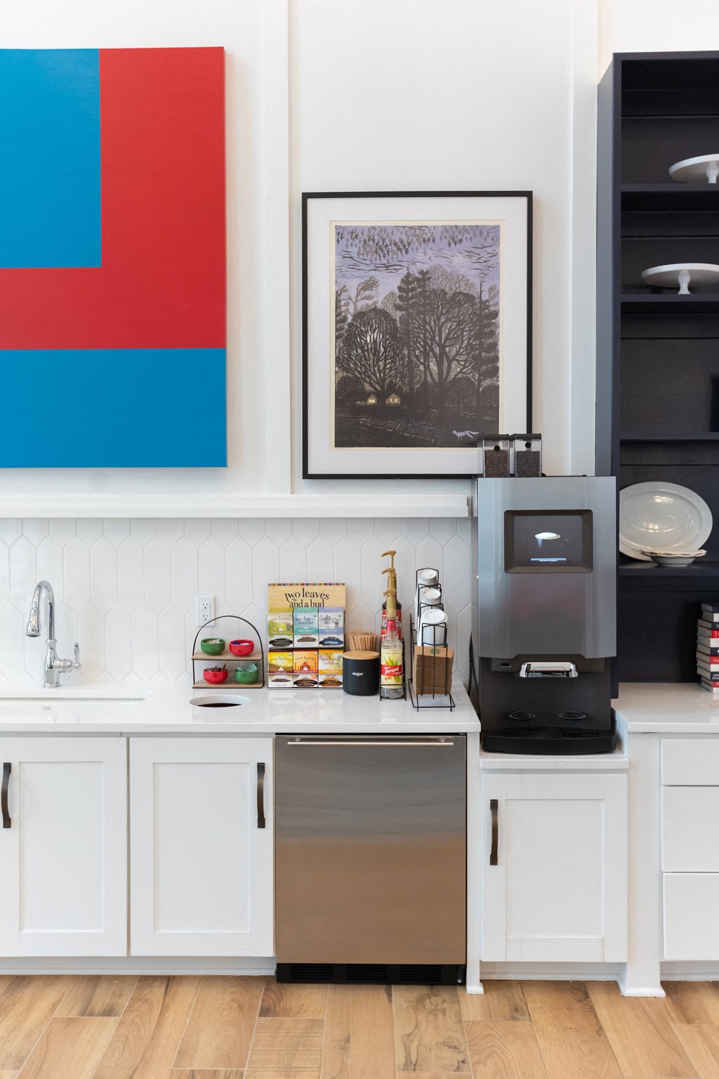 a kitchen with white cabinets and a red and blue painting on the wall