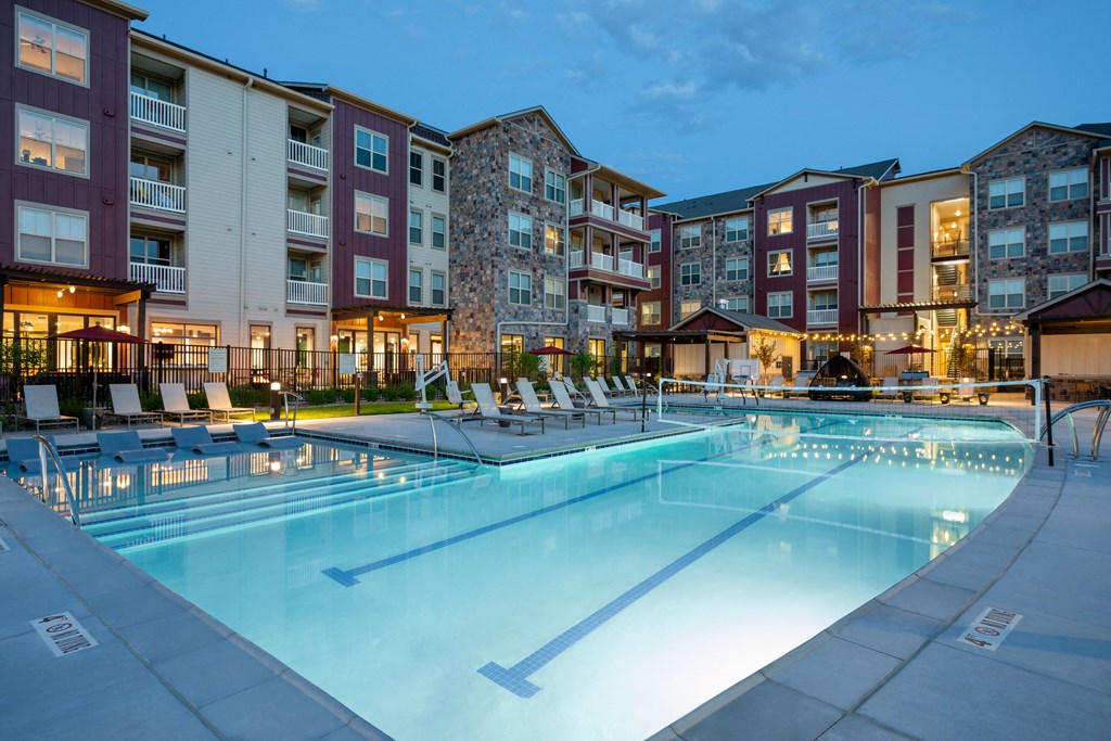 a swimming pool at night with an apartment building in the background