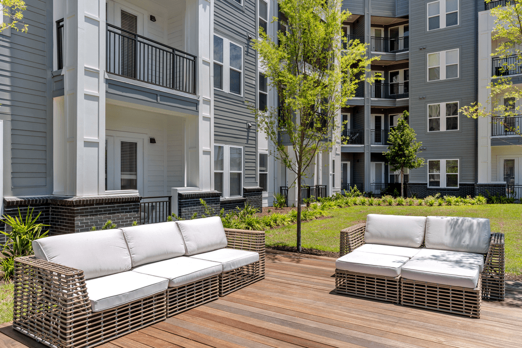 Two wicker sofas on a wooden deck in front of apartment buildings.