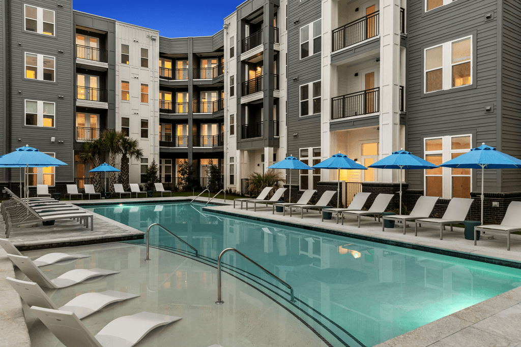 A swimming pool surrounded by lounge chairs and umbrellas in front of a modern apartment building.