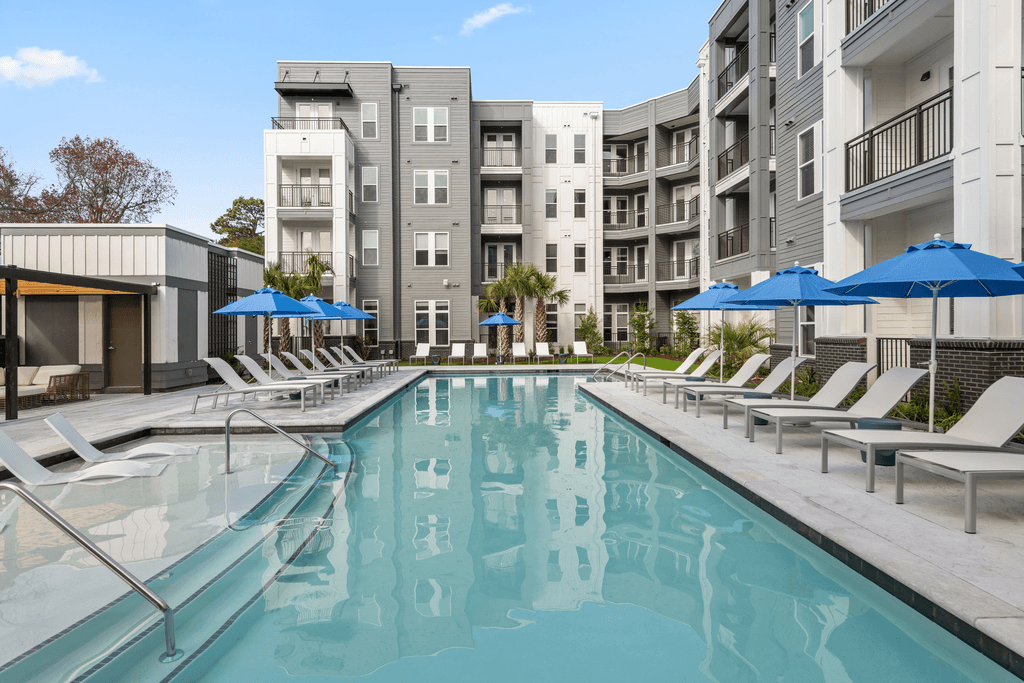 A large swimming pool with lounge chairs and umbrellas in front of apartment buildings.