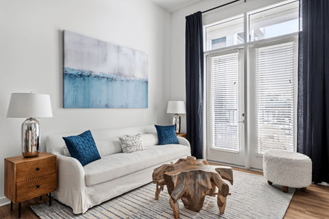 A living room with a white couch, a wooden side table, and a large painting on the wall.