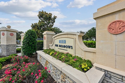 A sign that says "The Meadows" is in front of a wall with flowers.