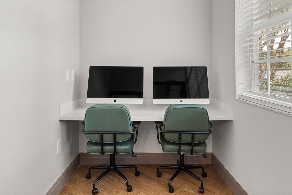 Two computer monitors are sitting on a desk with green chairs.