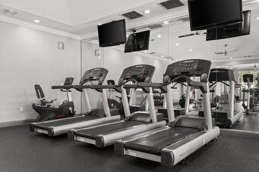 A gym with treadmills and televisions mounted on the wall.