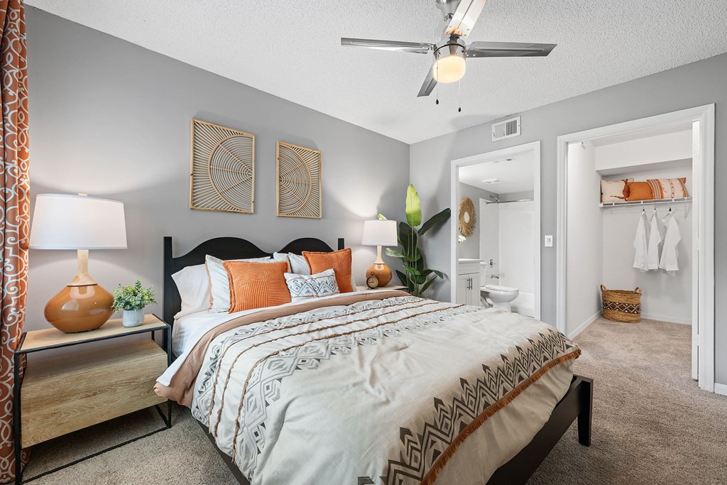 A bedroom with a bed, a ceiling fan, and a nightstand with a lamp.