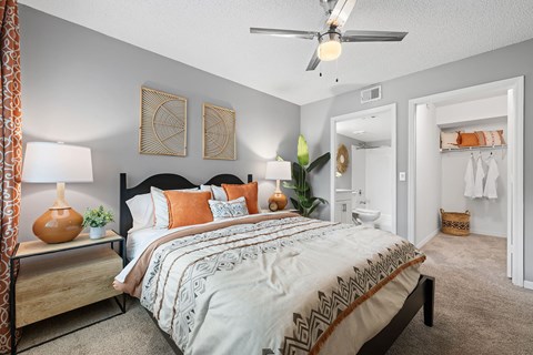 A bedroom with a bed, a ceiling fan, and a nightstand with a lamp.