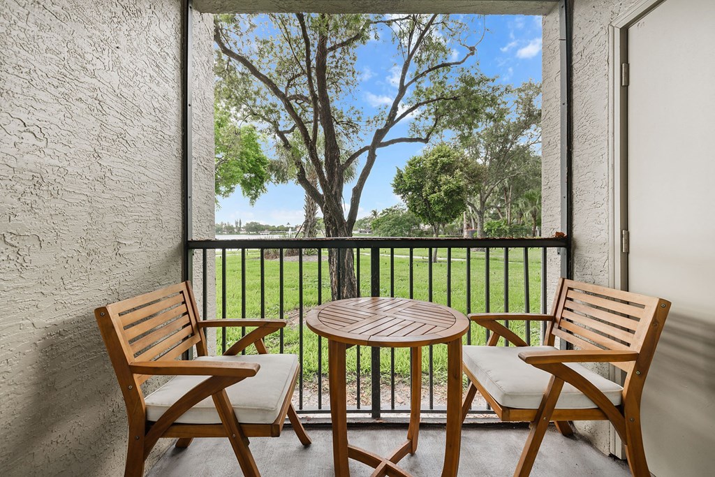 A patio with a table and two chairs overlooking a green lawn.