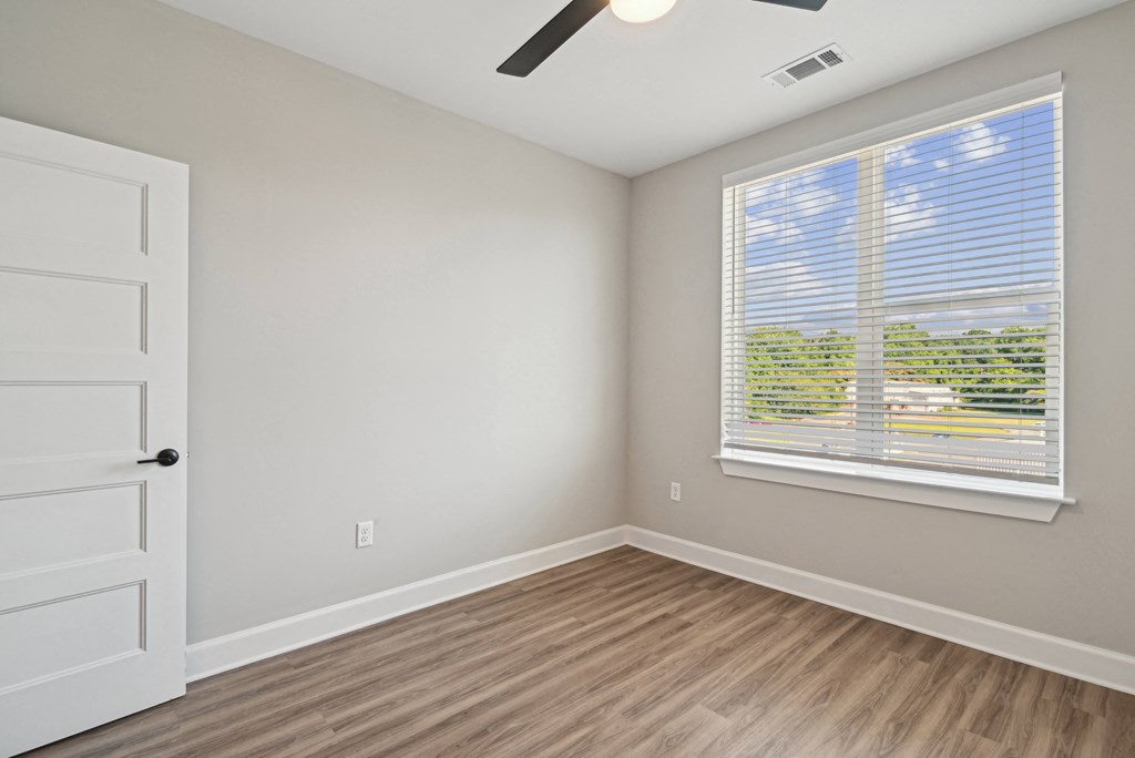 an empty bedroom with a large window and wooden floors