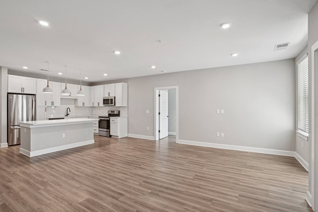 a renovated living room and kitchen with white walls and wood flooring