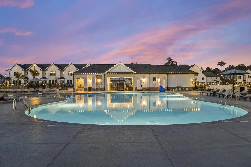 A large swimming pool in front of a building with lights on.