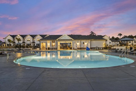 A large swimming pool in front of a building with lights on.