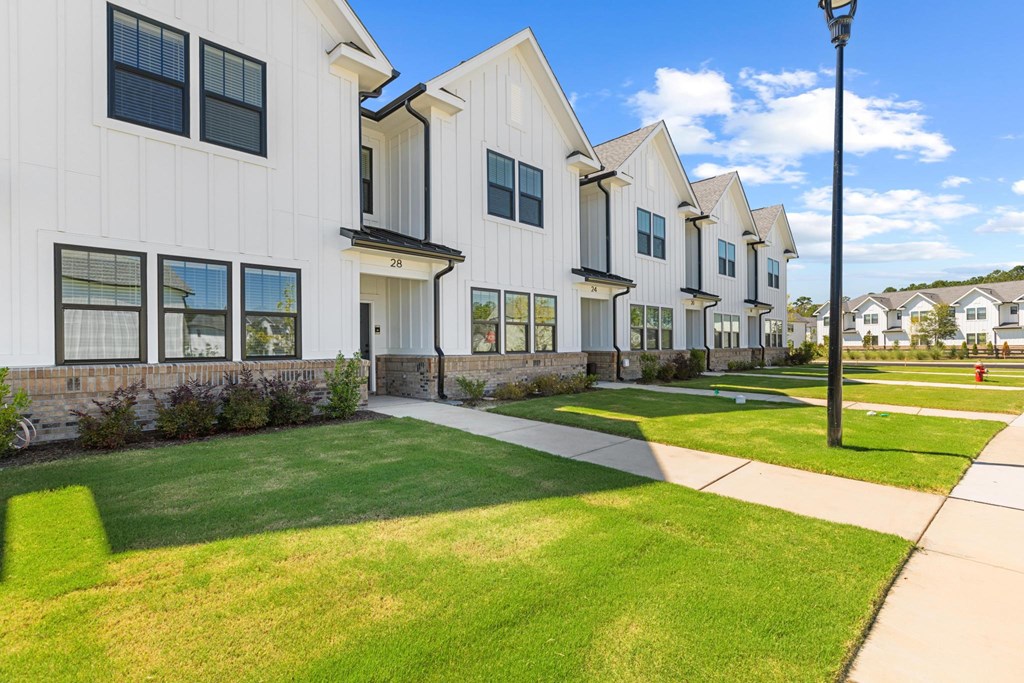 A white building with black trim and windows is surrounded by a grassy area.