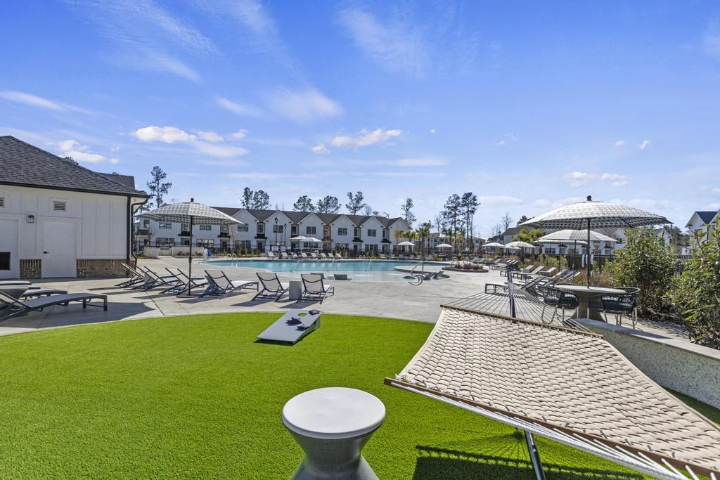 A grassy area with a hammock and a pool behind it.