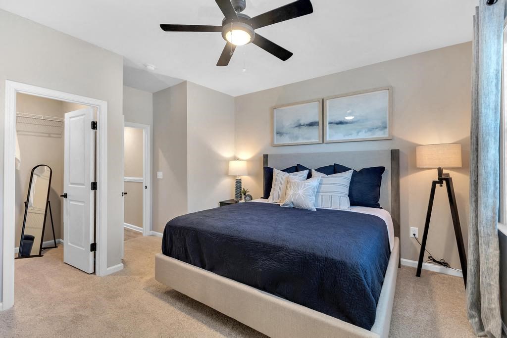 A bedroom with a bed, a ceiling fan, and a nightstand with a lamp.