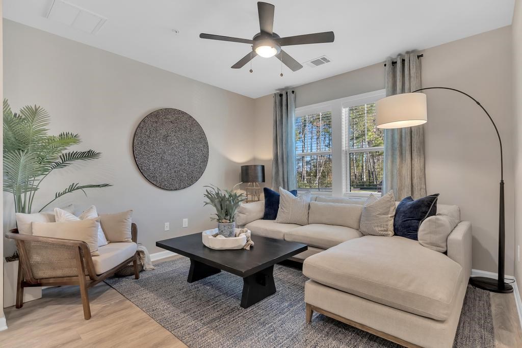 A living room with a beige couch, a wooden chair, a coffee table, and a ceiling fan.