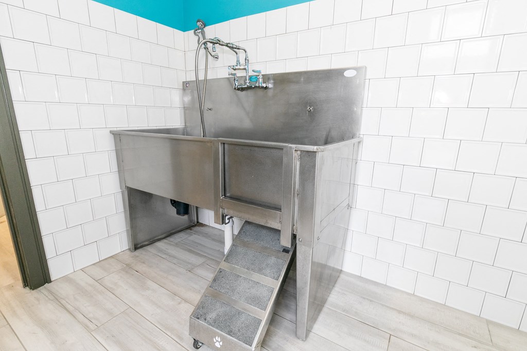 a large stainless steel sink in a white tiled room with a faucet