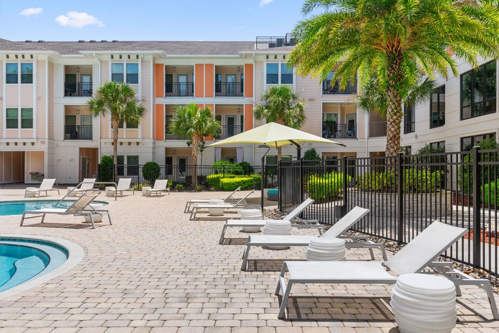 a pool with lounge chairs and a umbrella in front of an apartment building