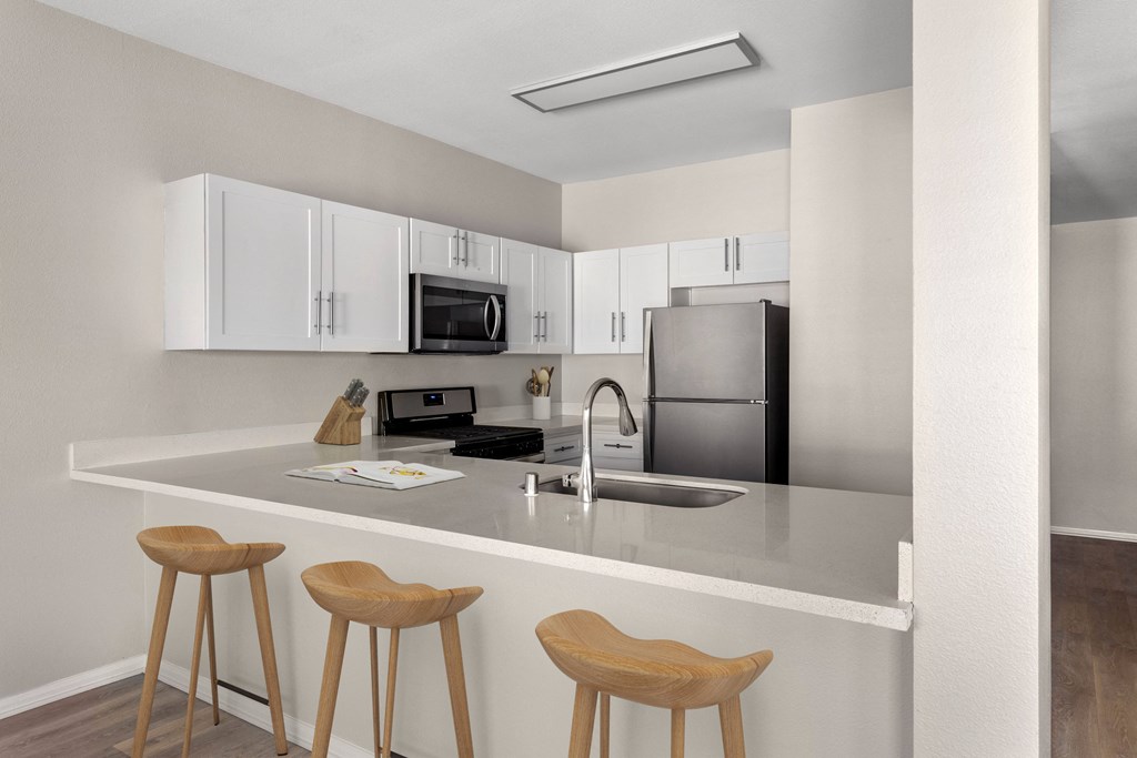 a kitchen with white cabinets and a counter with three stools