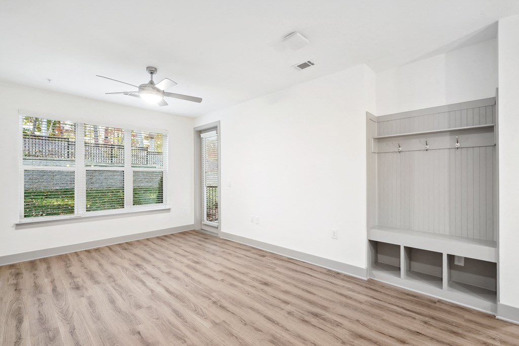 an empty living room with a large window and a ceiling fan