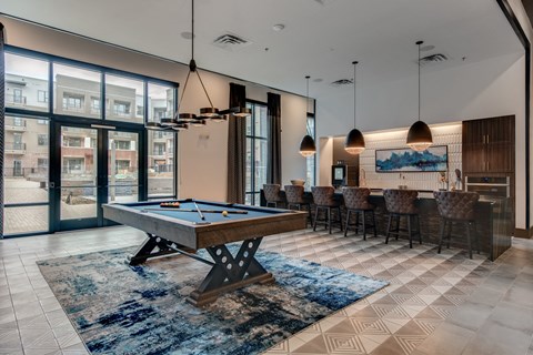 A pool table is in the middle of a room with a view of apartment buildings outside.