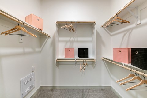 a walk in closet with shelves and hooks and a rack with pink and white boxes