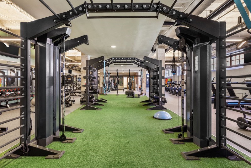 a green carpeted gym floor with a row of exercise equipment on the left and a row