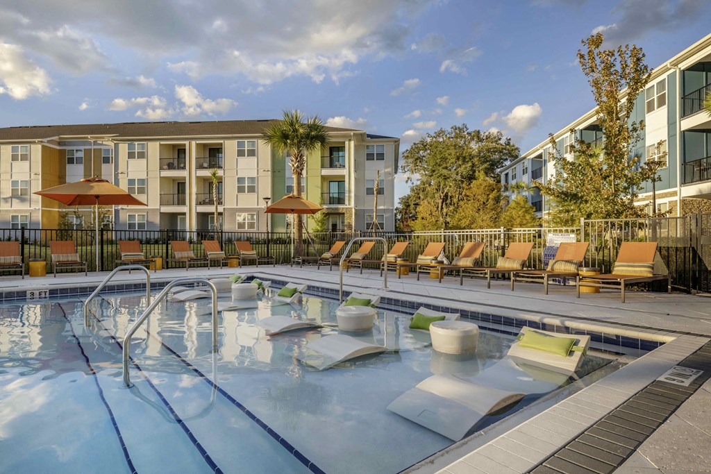 a swimming pool with chairs and umbrellas in front of an apartment building
