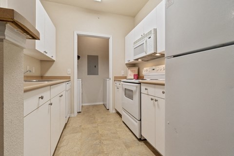 a long kitchen with white cabinets and appliances and a door to a hallway