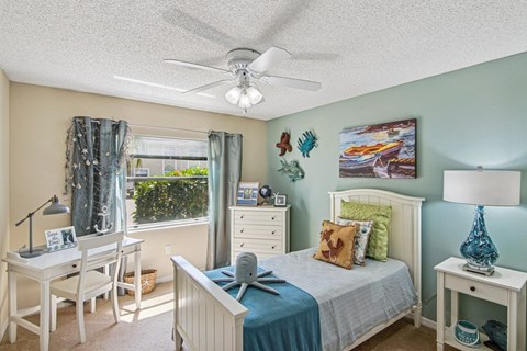 A bedroom with a bed, desk, chair, and window.