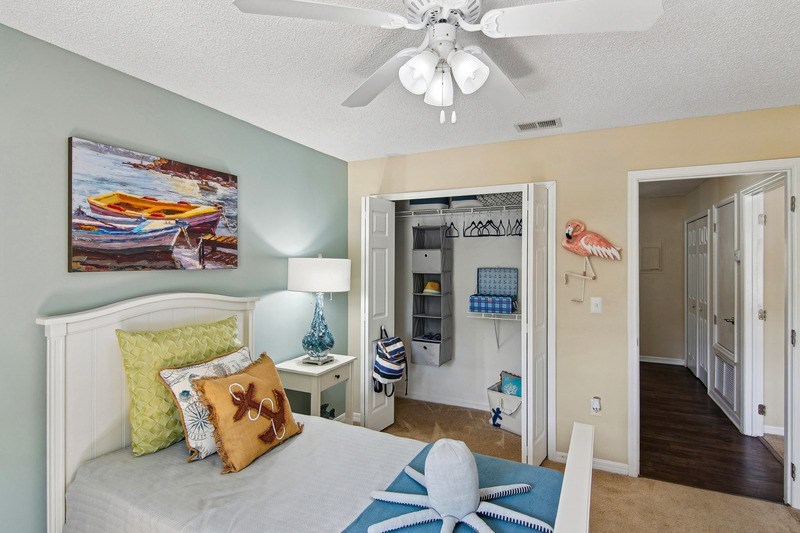 A bedroom with a bed, a ceiling fan, and a painting on the wall.