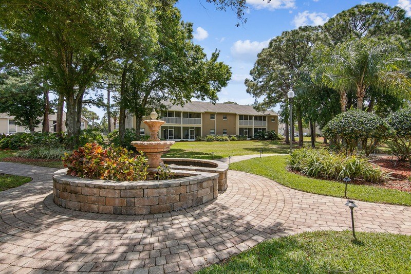 A circular brick walkway leads to a building with a fountain in the middle.