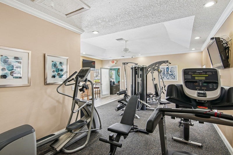 A gym with an  elliptical machines and a television.