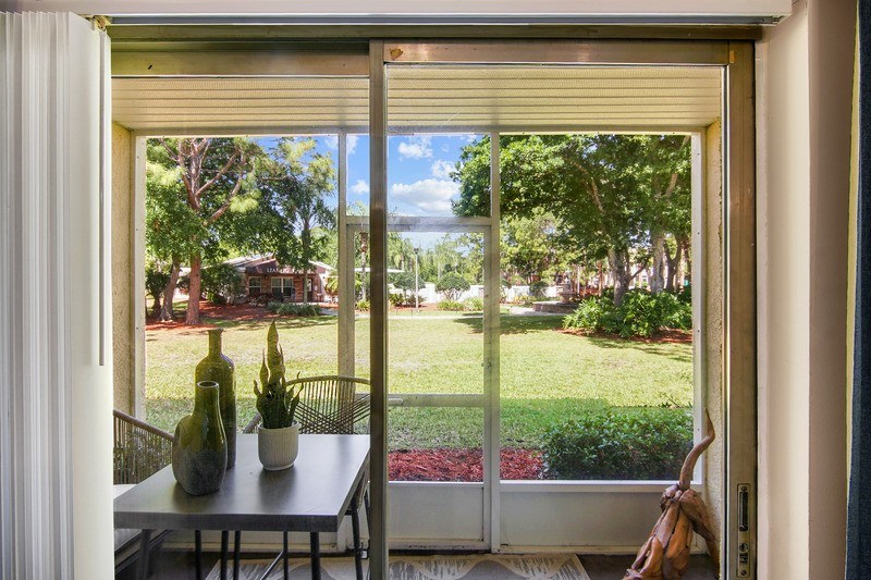A table with a vase and a plant on it sits in front of a sliding glass door.