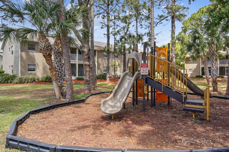A playground with a slide and a building in the background.